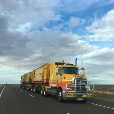 Żółty road train na pustej drodze. Kierowca tira zarabia, pokonując długie dystanse.