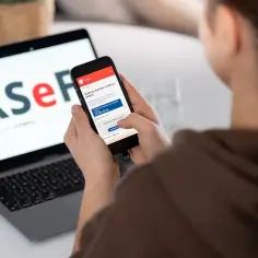 Kobieta korzysta z telefonu z aplikacją KSeF, gdzie widnieje informacja o fakturze ustrukturyzowanej. Laptop obok wyświetla logo KSeF.