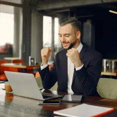 Uśmiechnięty key account manager cieszy się z sukcesu przy laptopie w kawiarni.
