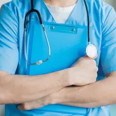 Lekarz rodzinny w niebieskim kitlu trzyma teczkę i stetoskop. Zastanawiasz się, ile zarabia lekarz rodzinny?