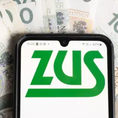 Telefon z logo ZUS na tle banknotów 100 zł. Sprawdź aktualną stopę procentową składek na ubezpieczenie wypadkowe.