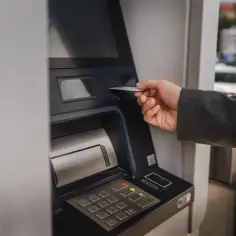 Dłoń wsuwa kartę do bankomatu, by sprawdzić, ile można wypłacić.