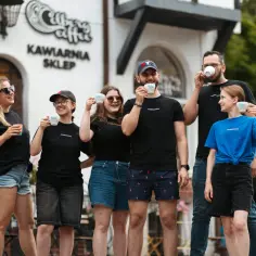 Uśmiechnięty zespół barista przed kawiarnią, każdy z filiżanką kawy.
