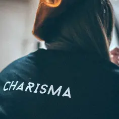 Osoba w bluzie z napisem "CHARISMA" na plecach, z włosami opadającymi na ramiona.