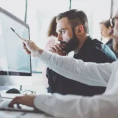 Analityk biznesowy wskazuje na wykres na ekranie komputera, omawiając dane z kolegą.