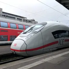 Biały pociąg ICE i czerwony pociąg regionalny stoją na stacji. Maszynista czeka na sygnał do odjazdu.