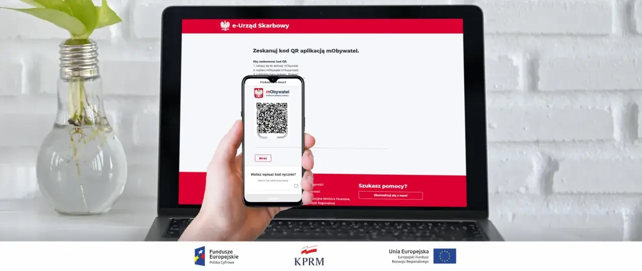 Dłoń trzyma smartfon z kodem QR do aplikacji mObywatel na ekranie laptopa z napisem e-Urząd Skarbowy. Ułatwia to szybkie załatwienie spraw, np. zwrot podatku.