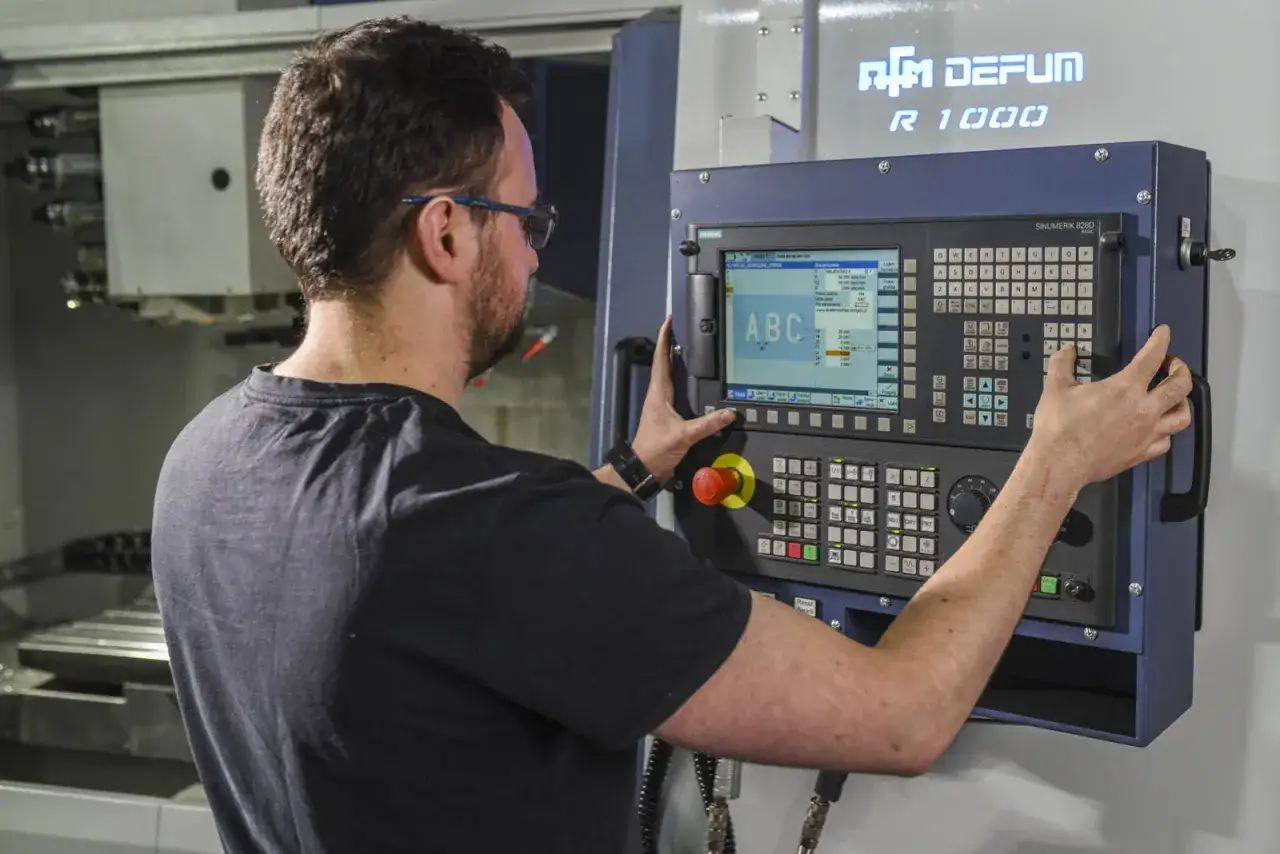 Operator CNC przy panelu sterowania maszyny DEFUM R 1000, wprowadzający dane na ekranie.