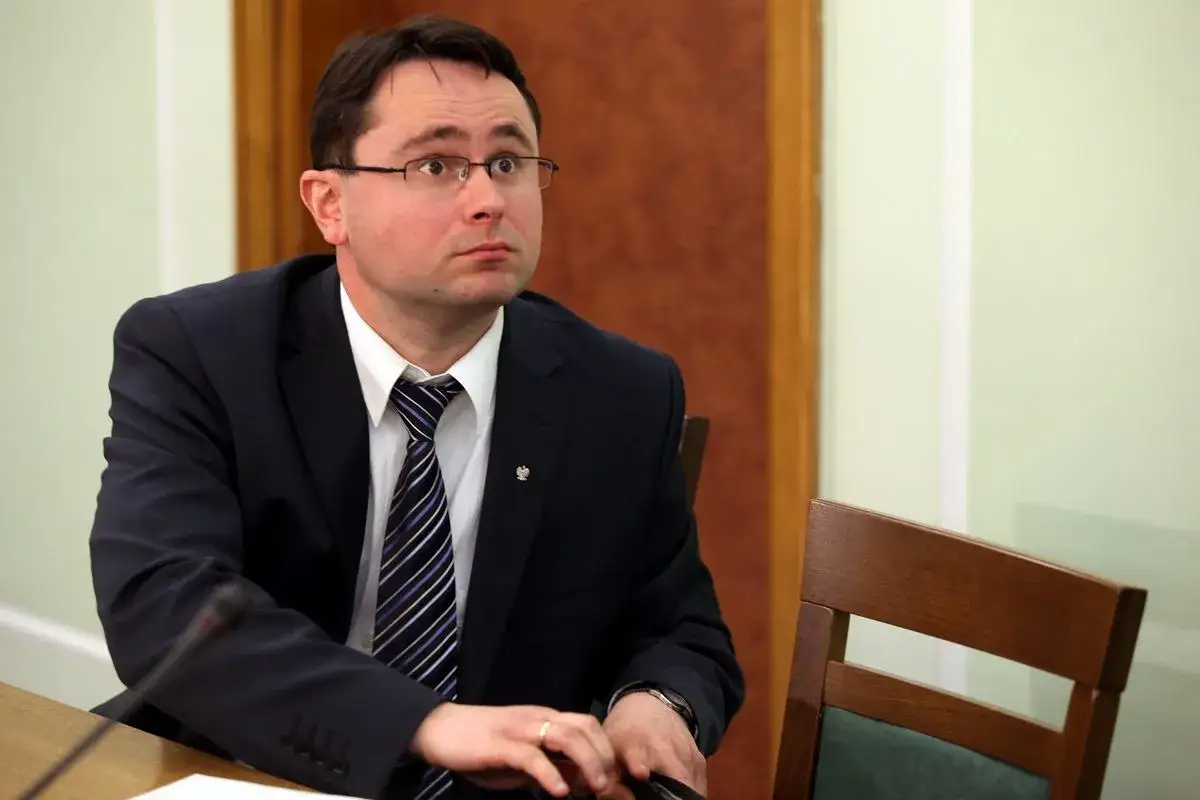 Mężczyzna w garniturze i okularach, siedzący przy stole, zastanawia się, ile zarabia prokurator.