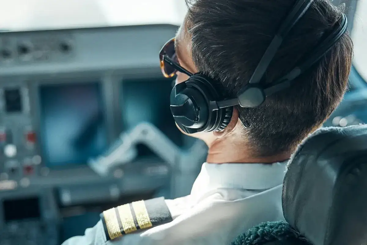 Pilot samolotu w słuchawkach i okularach przeciwsłonecznych, siedzący w kokpicie.