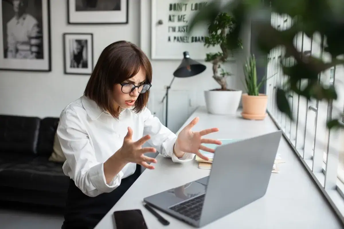 Kobieta z osobowością anankastyczną, z okularami, gestykuluje z frustracją przed laptopem.