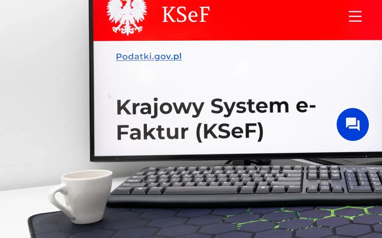 Monitor z logo KSeF i orłem, klawiatura i filiżanka. System KSeF ułatwia rozliczenia z fiskusem.