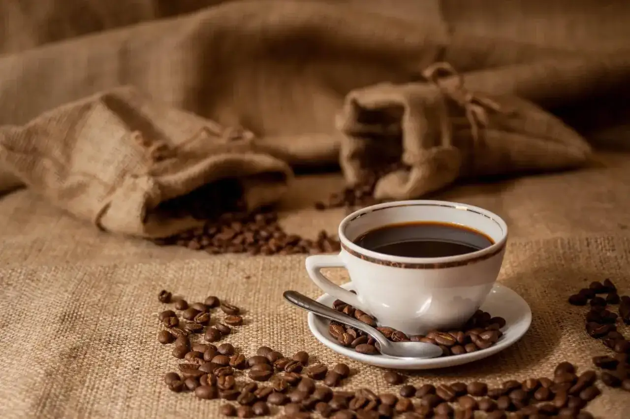 Aromaticzne ziarna kawy rozsypane wokół filiżanki. W tle dwa worki z kawą, jakby przygotowane przez doświadczonego baristę.